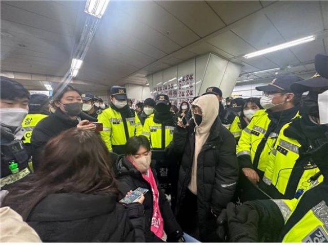 휠체어 이용자를 위한 ‘이동식 발판’이 장애인 활동가의 탑승을 저지하는 도구로 기능하고 있는 모습. 원래 이동식 발판은 승강장과 지하철 사이 틈이 넓거나 단차가 생기는 경우 휠체어 바퀴가 틈에 빠지지 않게 하기 위해 만들어졌다.